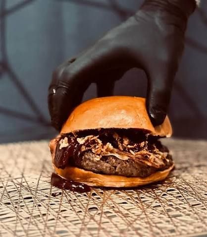 Hamburguesa de Nono's Burgers con pan brioche, carne a la brasa y salsa, sujetada con un guante negro